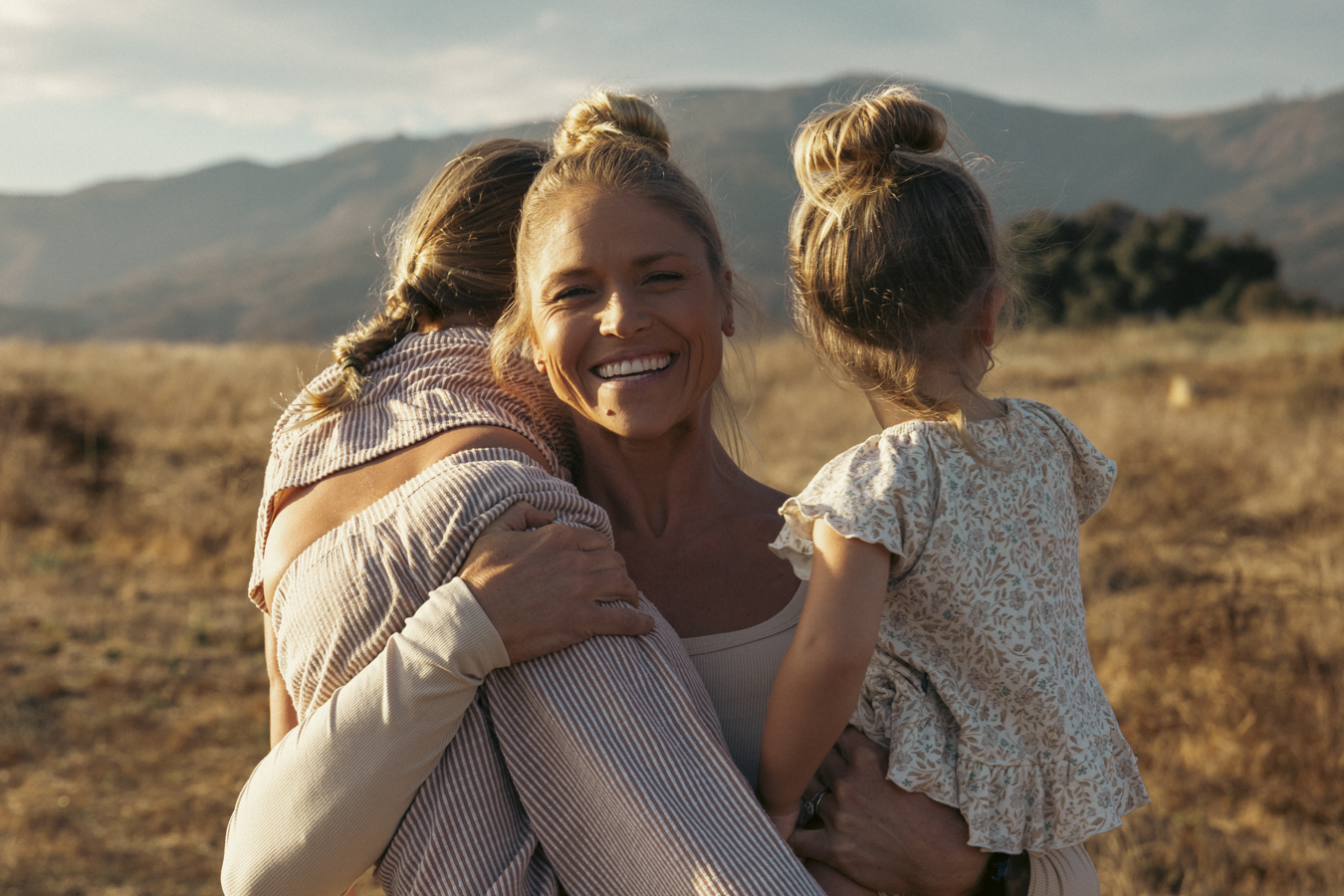 Anne Marie carrying her two kids in a golden field at sunset